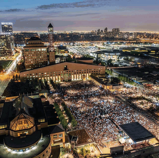 an aerial view of a city at night with a large crowd gathered in front of a large building with a clock tower