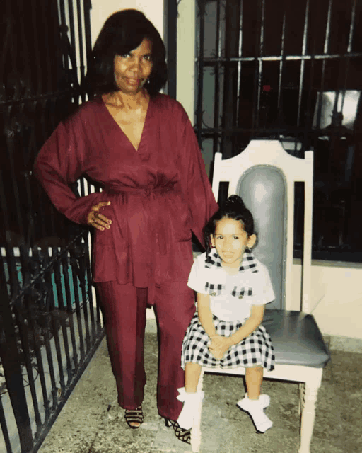 a woman in a maroon suit stands next to a little girl sitting in a chair