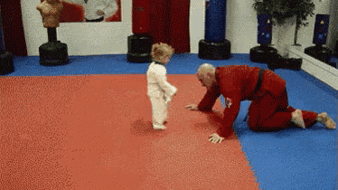 a man in a red karate uniform is kneeling down next to a small child in a white karate uniform .