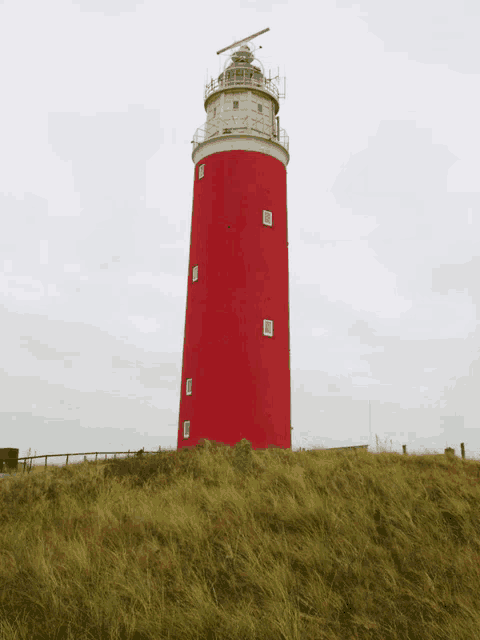 a red and white lighthouse sits on top of a grass covered hill