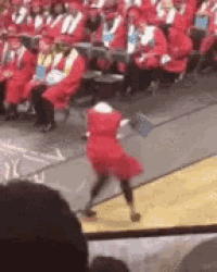 a girl in a red dress is dancing on a stage in front of a crowd of people in graduation caps and gowns .