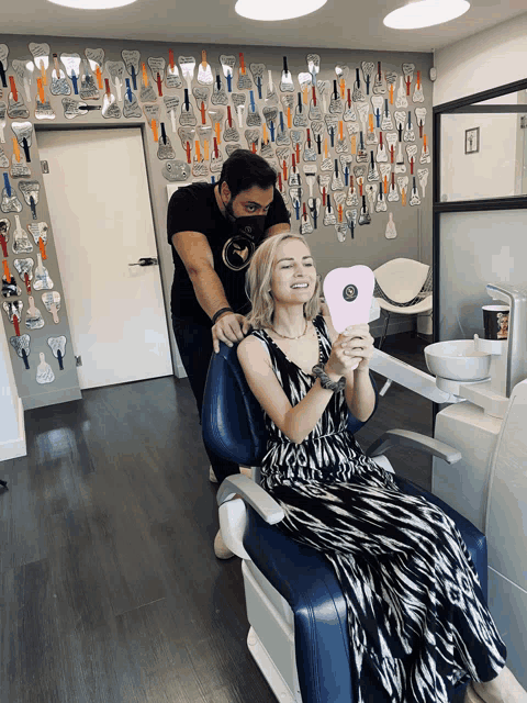 a woman is sitting in a dental chair looking at her smile in a mirror