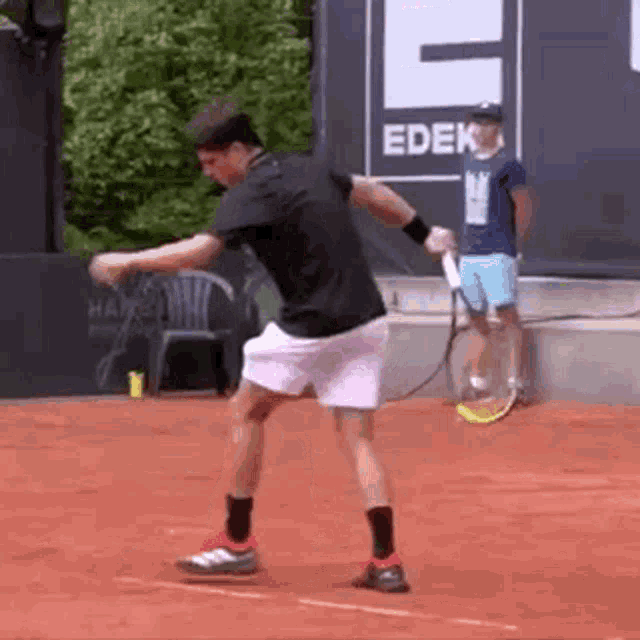 a man is swinging a tennis racket on a tennis court in front of a sign that says edek .