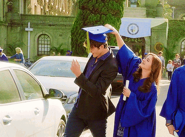 a woman in a blue graduation gown is holding a diploma while a man in a black suit holds a graduation cap