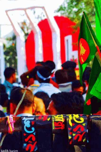 a crowd of people are gathered in front of a red white and green sign that says ' sadik karim '