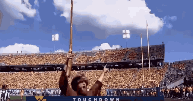 a man in a cowboy hat holds up a flag in front of a stadium that says touchdown on the bottom