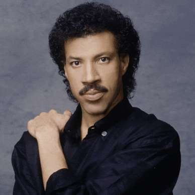 a man with curly hair and a mustache is standing with his arms crossed