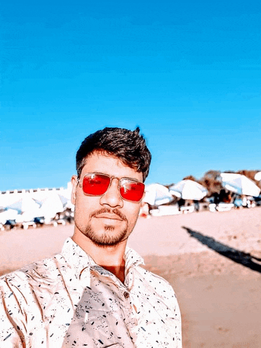 a man wearing red sunglasses takes a picture of himself on the beach