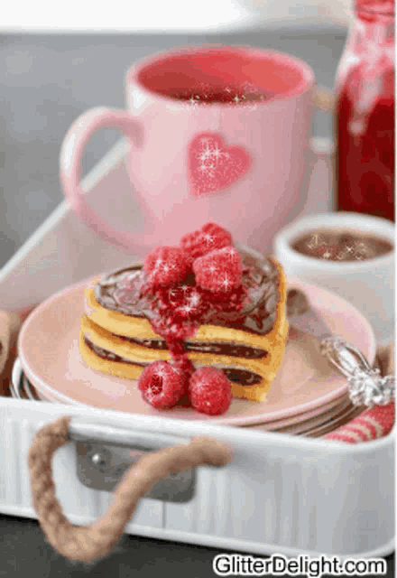 a pink mug with a heart on it sits next to a pink plate with a piece of cake and raspberries on it