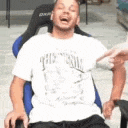 a man in a white shirt is sitting in a chair with his mouth open .