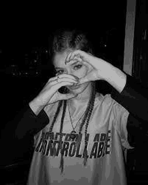 a woman is making a heart shape with her hands while drinking from a bottle .