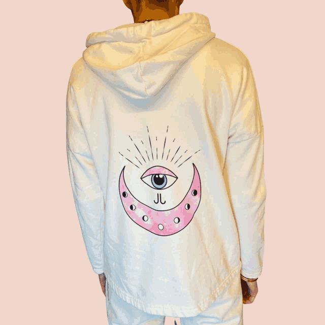 a person is wearing a white hoodie with a pink crescent moon and an eye on it