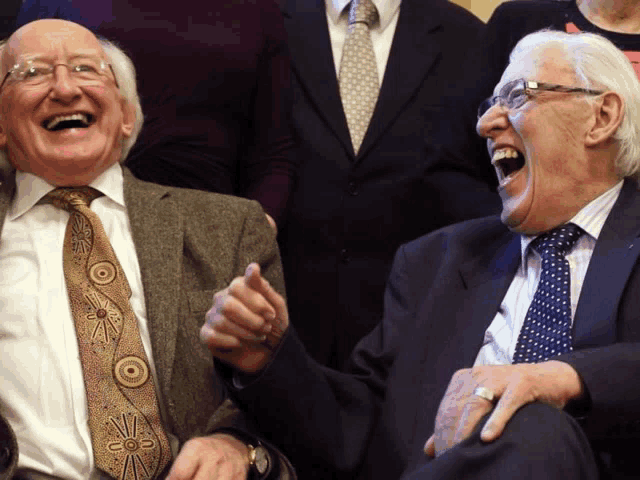 two men in suits and ties laugh together