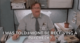 a man is sitting at a desk in an office talking to someone while wearing glasses and a tie .