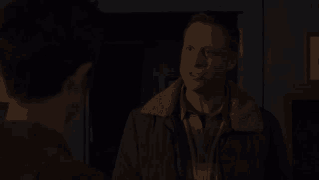 two men are standing next to each other in a dark room and talking to each other .