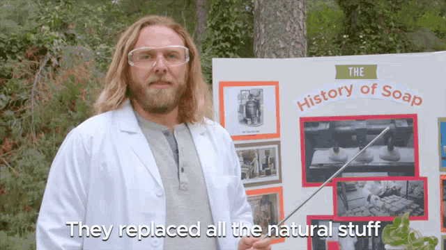 a man in a lab coat holds a stick in front of a sign that says the history of soap