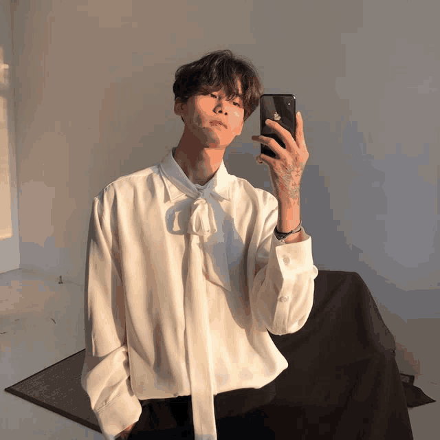 a man in a white shirt taking a selfie with his phone