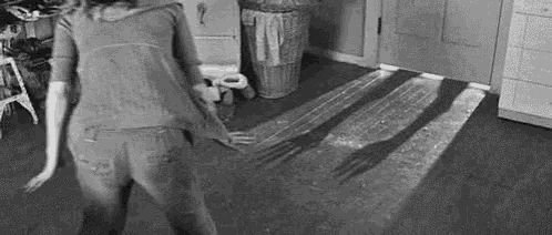 a black and white photo of a woman dancing in a kitchen with a shadow of a fork on the floor .