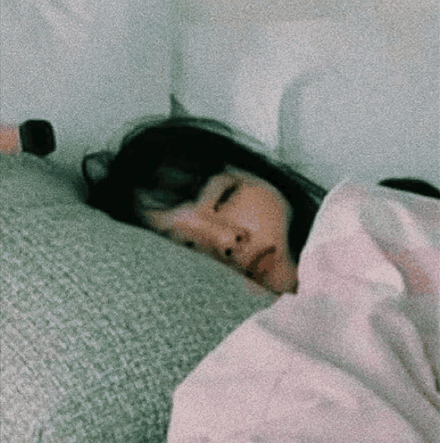 a woman is sleeping in a bed with her eyes closed and a pink blanket .