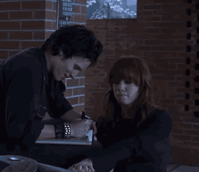 a man and a woman are sitting in front of a brick wall with a sign that says service for friends