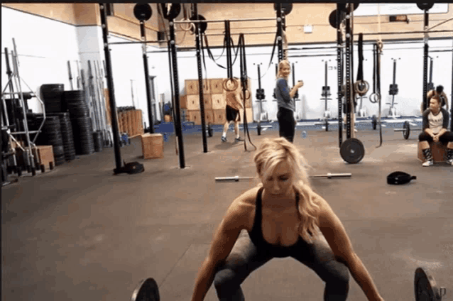 a woman in a black tank top is doing squats in a gym with other women