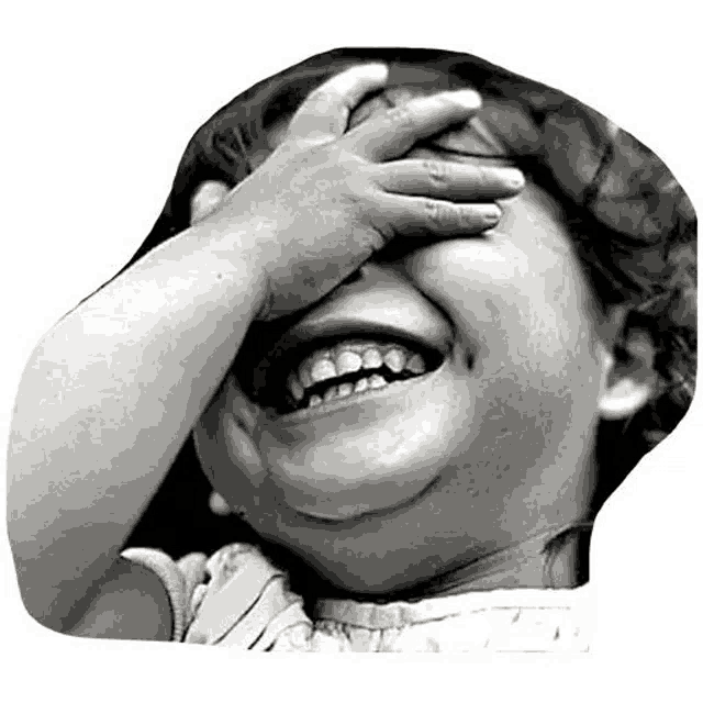 a black and white photo of a little girl covering her eyes with her hand while laughing .