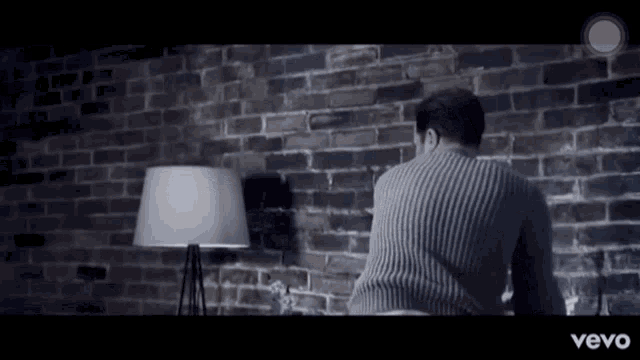 a man in a sweater is sitting in front of a brick wall in a vevo ad