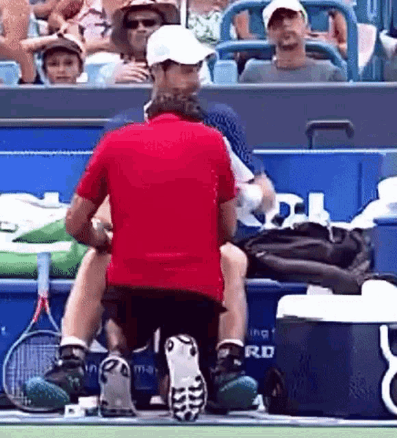 a man in a red shirt is kneeling down on a tennis court while a woman holds a tennis racquet .