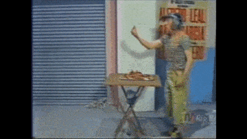 a man is standing in front of a table with a pizza on it and giving a thumbs up .