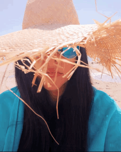 a woman wearing a straw hat and sunglasses looks at the camera