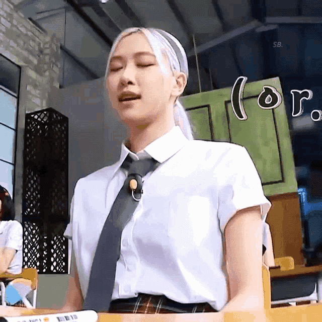 a woman in a school uniform and tie is sitting at a desk in a classroom .