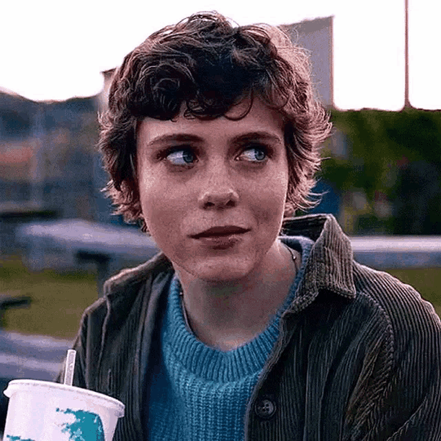 a young woman is sitting at a table holding a drink and a straw .