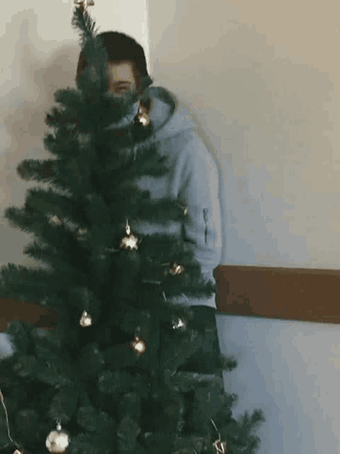 a man is hiding behind a christmas tree while wearing a mask