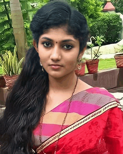 a woman wearing a red and pink striped saree with a gold chain around her neck