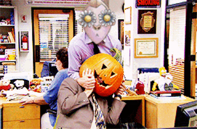 a man is holding a pumpkin in front of his face in an office with a smoking sign on the wall