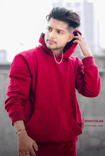 a young man wearing a red hoodie with a pearl necklace around his neck looks at the camera