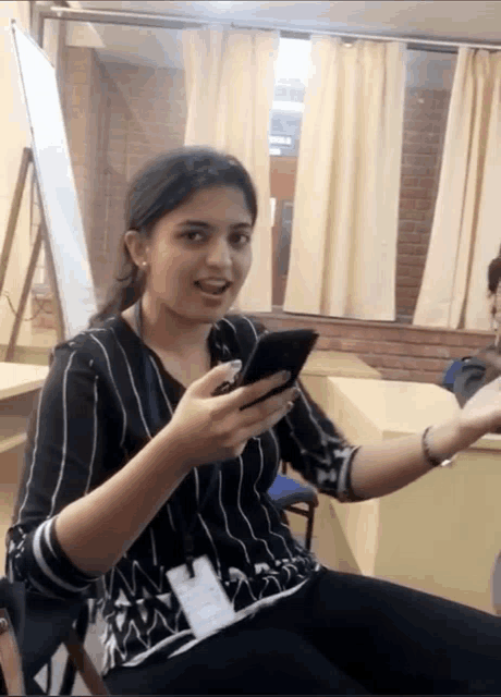 a woman in a black and white striped shirt is holding a cellphone