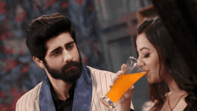 a man with a beard and a woman drinking a glass of orange juice