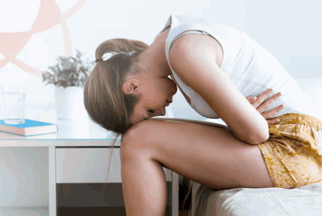 a woman sits on a bed with her head on her knees holding her stomach