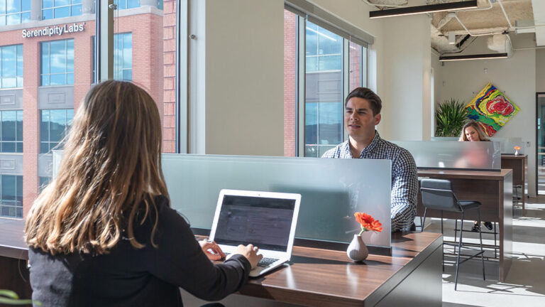 Members working in the Coworking area with a view of the Serendipity Labs logo peaking through the window.