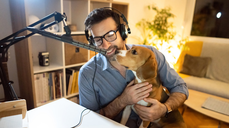 A man is facing a microphone with his pet beagle in his lap also facing the mic