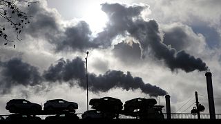 Rauch steigt aus einer Fabrik auf, als ein mit Autos beladener Lastwagen eine Brücke in Paris, Frankreich, überquert.