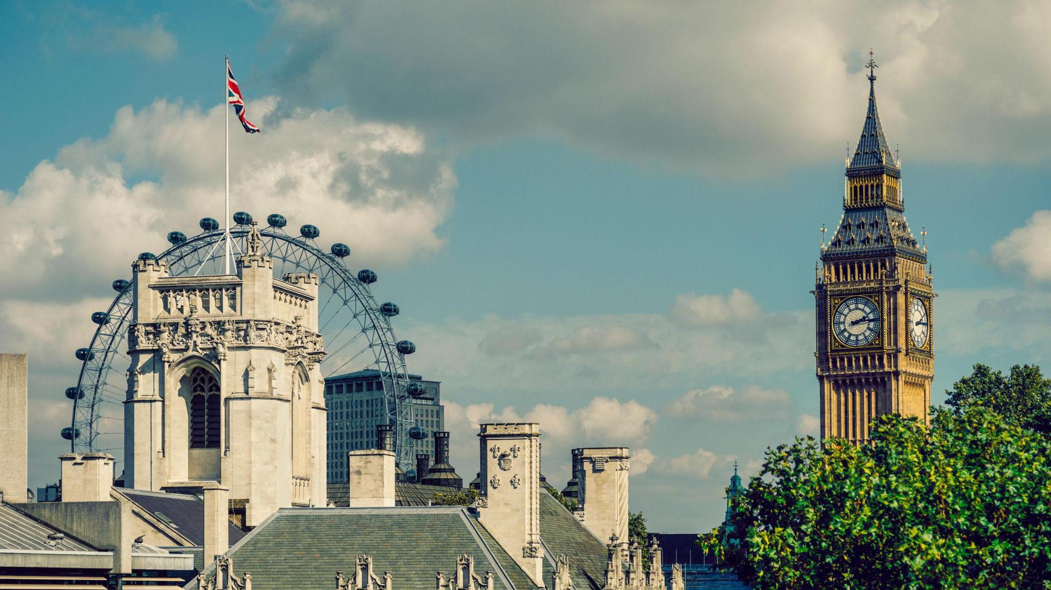 An image of London which includes the tower of the Supreme Court in the foreground with Big Ben in the background. The London Eye can be seen in the background behind the court building and there are trees in full bloom in the foreground.