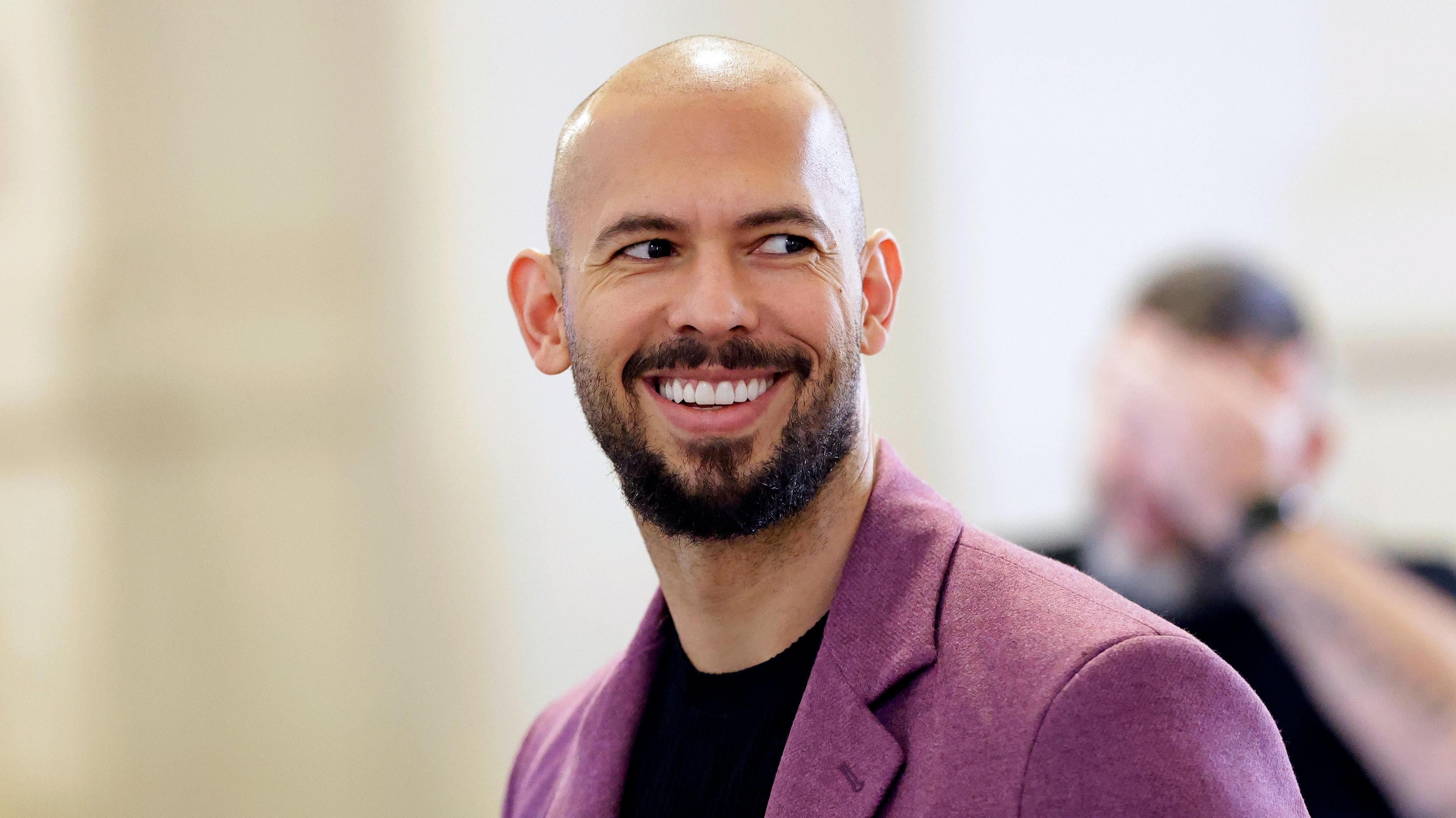 Photograph of Andrew Tate smiling and wearing a purple blazer