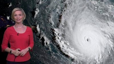 Weather presenter next to satellite image of a tropical cyclone