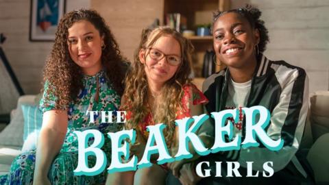 The Beaker Girls, three women and girls, from left to right there is an older woman with curly black hair, a young blonde girl wearing glasses, and a teenage black girl wearing a tracksuit and smiling brightly.