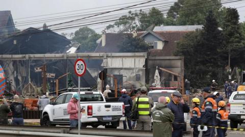 Emergency workers attend burned out buildings behind police tape at the scene of the crash.