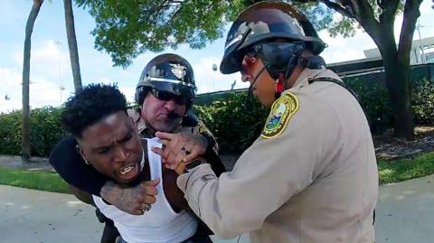 Hill with two officer grappling with him as he is handcuffed