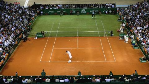  Federer serving in a match being played on a half-grass half-clay court