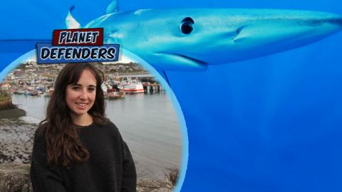 Megan smiles by the coast, a picture of a blue shark in the background.